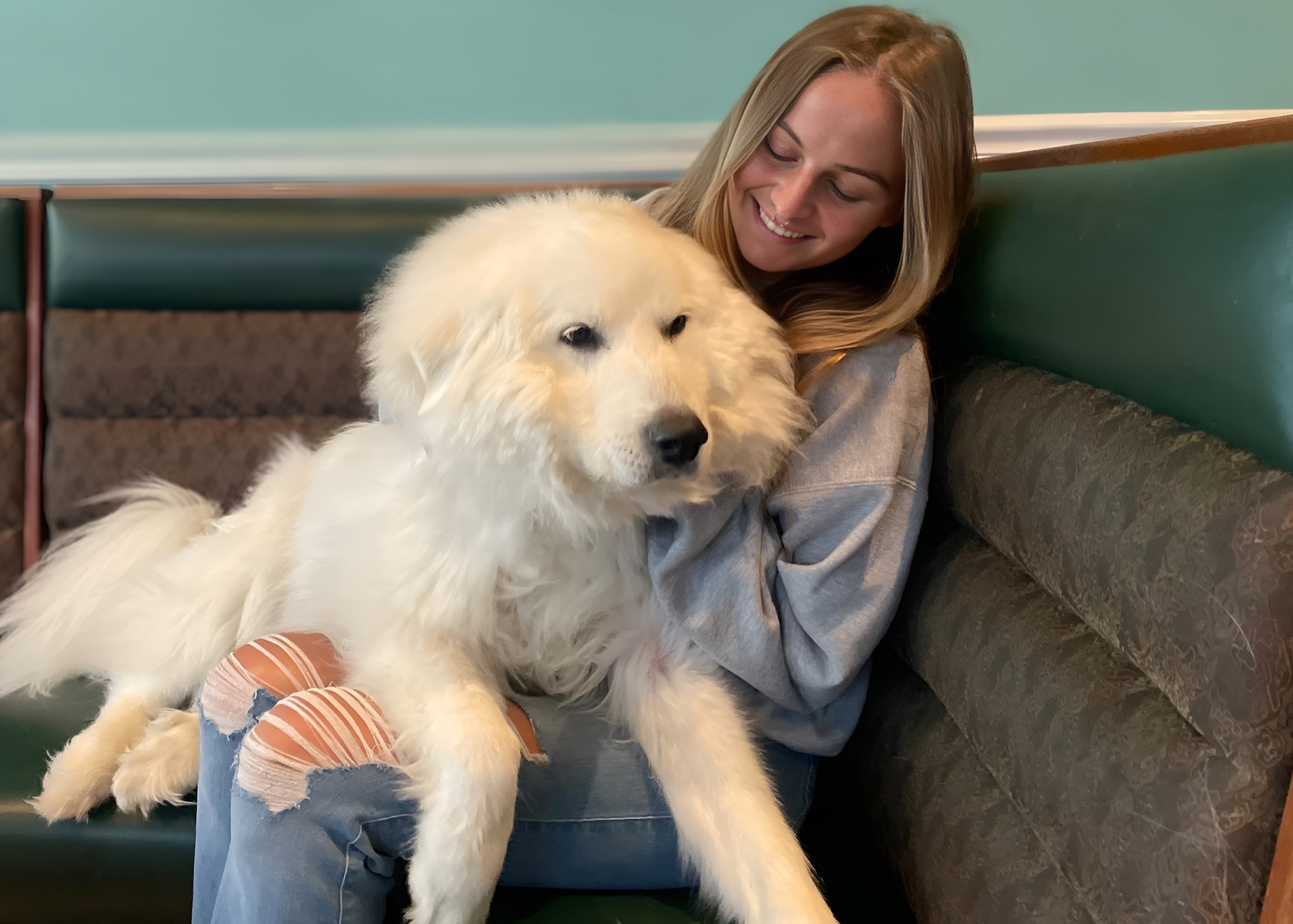 China the bar mascot, a white Great Pyrenees dog, and her owner Colby, the bar manager, sitting on the couch at Midtown Kava Lounge while smiling